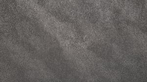 Textura de superficie tipo molcajete en primer plano, con acabado rugoso y granulado. Predominan tonos grises irregulares que crean una apariencia sobria, industrial y uniforme.