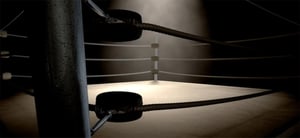 Interior de un cuadrilátero de boxeo visto desde una esquina, con cuerdas tensadas y postes oscuros. El ring está iluminado tenuemente, destacando el piso claro y creando un ambiente deportivo y dramático.